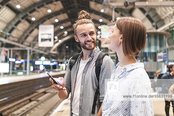 Junges Paar wartet am Bahnhof auf den Zug und benutzt ein Smartphone  Berlin  Deutschland