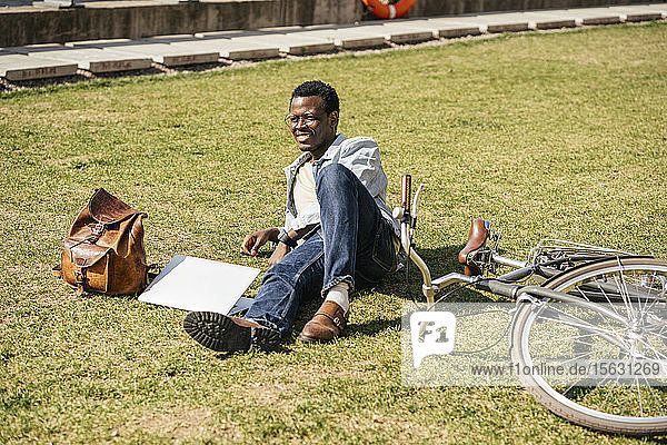 Junger Mann mit Alptop und Fahrrad  auf Gras liegend
