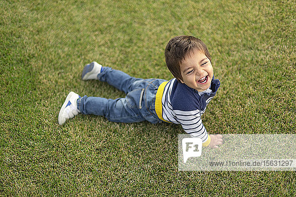 Porträt eines lachenden kleinen Jungen  der auf dem Rasen liegt
