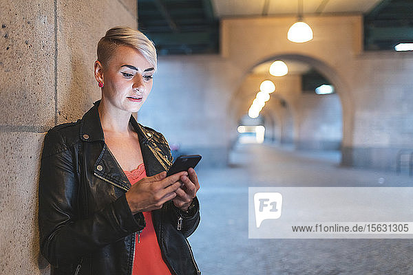 Porträt einer blonden Frau  die abends auf ein Smartphone schaut  Berlin  Deutschland