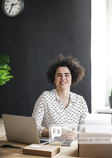 Porträt einer lächelnden jungen Frau  die im Büro am Schreibtisch sitzt