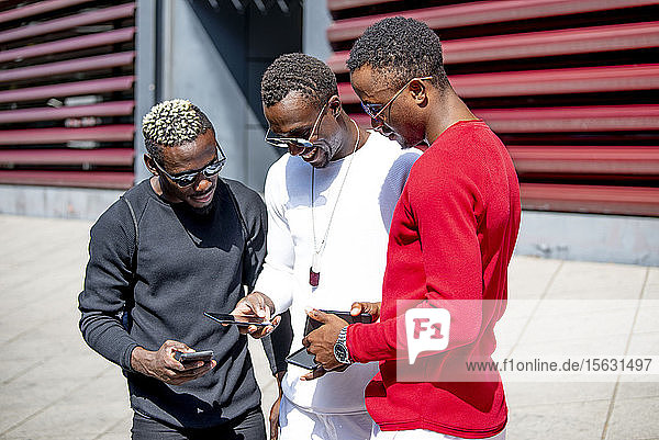 Drei coole junge Männer benutzen Mobiltelefone in der Stadt