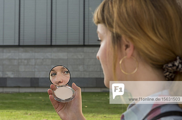 Junge Frau mit Nasenpiercing betrachtet Schönheitsspiegel in ihrer Hand