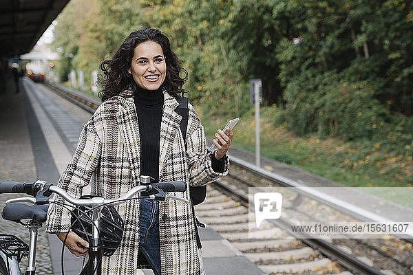 Smiling woman with bicycle and cell phone on an underground station platform  Berlin  Germany