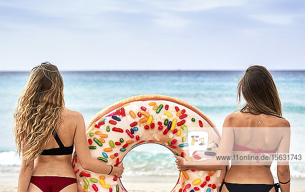 Zwei junge Frauen stehen vor dem Meer und halten einen großen aufblasbaren Ring