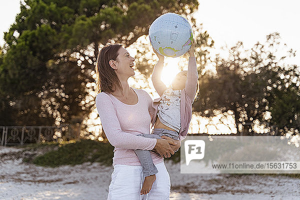 Mutter und kleine Tochter spielen zusammen mit Earth Beachball bei Sonnenuntergang