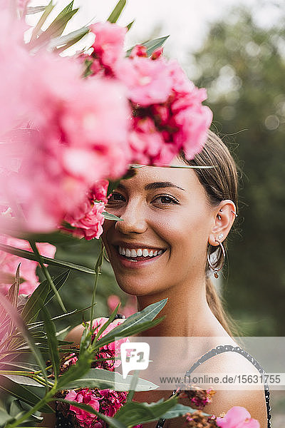 Porträt einer lachenden jungen Frau in einem Park mit rosa blühenden Blumen