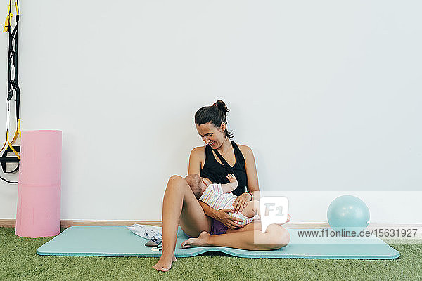 Junge Mutter sitzt auf Yogamatte und stillt ihr Baby