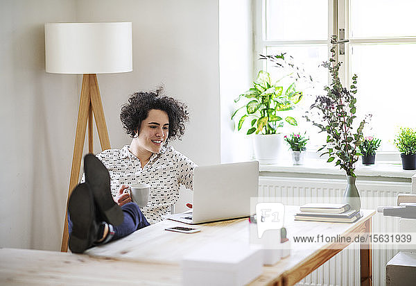 Entspannte junge Frau arbeitet am Schreibtisch am Laptop