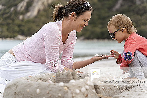 Glückliche Mutter und Tochter bauen eine Sandburg am Strand