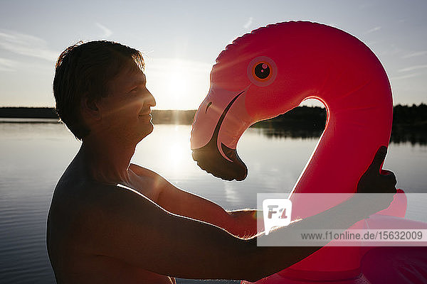 Junger Mann mit Flamingo-Pool schwebt bei Sonnenuntergang
