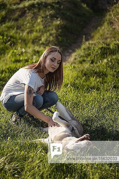 Porträt einer jungen Frau die ihren Hund auf einer Wiese streichelt