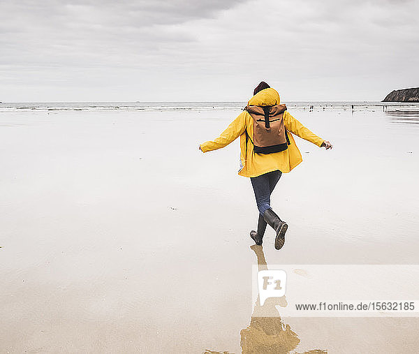 Junge Frau trägt gelbe Regenjacke und läuft am Strand  Bretagne  Frankreich