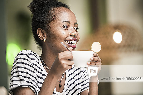 Porträt einer glücklichen jungen Frau die in einem Café eine Kaffeetasse hält