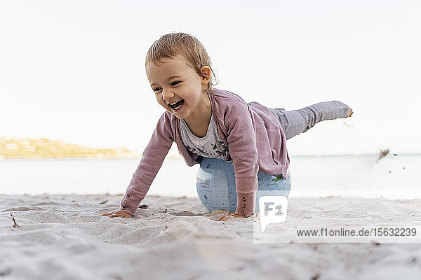 Porträt eines lachenden kleinen Mädchens  das auf einem Strandball der Erde balanciert