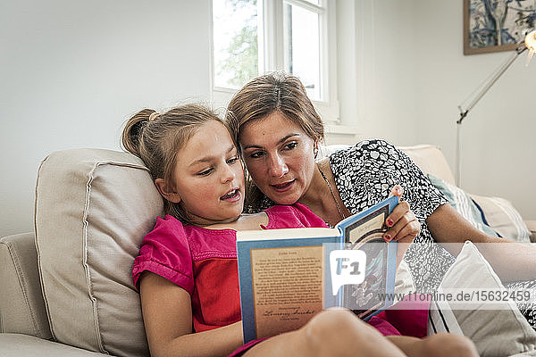 Mother reading book with daughter on couch in living room