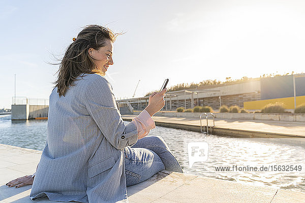 Glückliche junge Frau entspannt sich im Sonnenlicht und schaut auf ihr Handy  Barcelona  Spanien