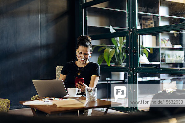 Lässige junge Geschäftsfrau mit Laptop und Smartphone im Loft-Büro