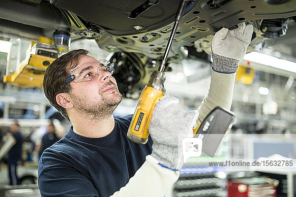 Mann arbeitet am Unterboden eines Autos in einer modernen Fabrik