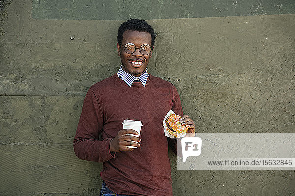 Junger Mann mit einem Chesseburger und Kaffee zum Mitnehmen  Portrait