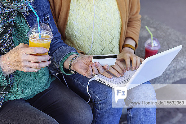 Zwei Frauen kaufen gemeinsam im Freien online ein