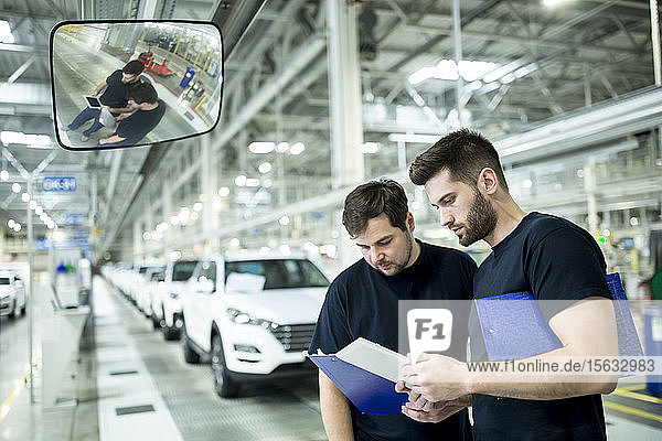 Zwei Kollegen arbeiten in einer modernen Autofabrik mit Zwischenablage und Tablett