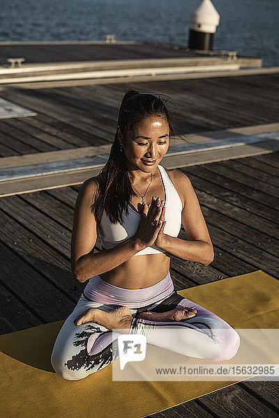 Asiatische Frau praktiziert Yoga auf einem Pier im Hafen