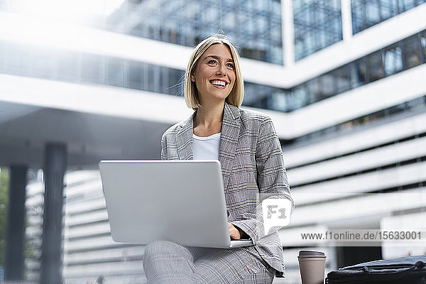 Lächelnde junge Geschäftsfrau mit Laptop in der Stadt