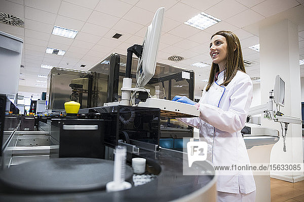 Junge Frau in weißer Kleidung benutzt Probenanalysegerät bei der Arbeit im Forschungslabor