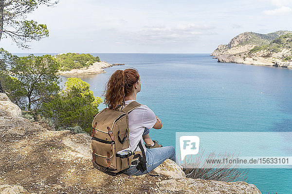 Rothaarige Frau sitzt auf einem Aussichtspunkt und schaut in die Ferne  Ibiza