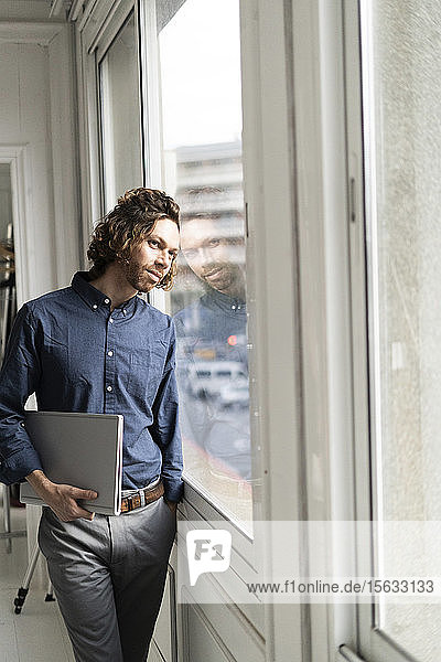 Mann hält Ordner in einem Studio und schaut aus dem Fenster