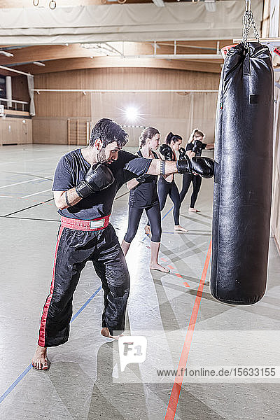Trainer und Boxerinnen trainieren am Boxsack in der Sporthalle