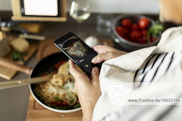 Nahaufnahme einer Frau,  die ein Smartphone-Foto von ihrem Nudelgericht in der heimischen Küche macht