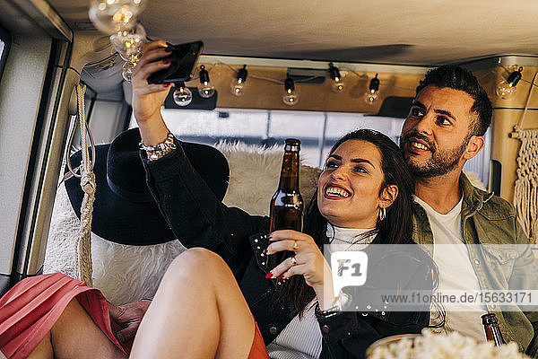 Happy young couple taking a selfie inside camper van