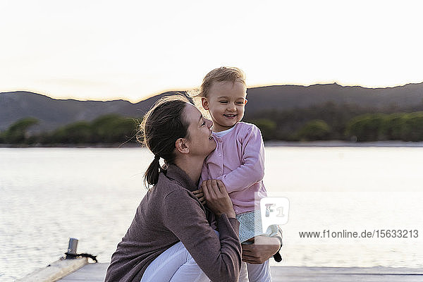 Glückliche Mutter hält ihre Tochter bei Sonnenuntergang auf einem Steg