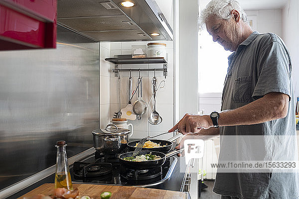 Älterer Mann bereitet in seiner Küche Essen in Bratpfannen zu