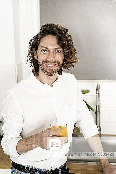 Porträt eines lächelnden Mannes mit einem Glas Orangensaft in der heimischen Küche