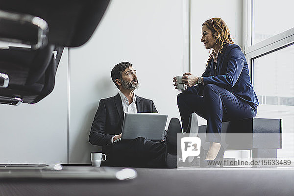Businesswoman with businessman in office sitting on the floor using laptop