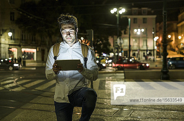 Porträt eines jungen Mannes mit digitalem Tablet und Kopfhörern in der Stadt bei Nacht Lissabon Portugal