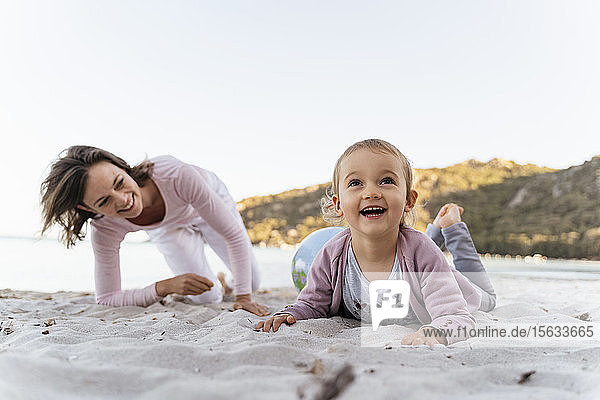 Porträt eines lächelnden  glücklichen Mädchens am Strand mit einer Mutter  die sie aus dem Hintergrund beobachtet