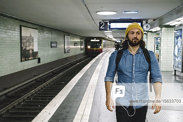 Portrait of man with backpack and earphones walking at platform  Berlin  Germany