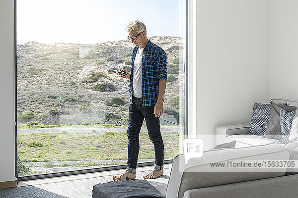 Gelegenheits-Geschäftsmann vor dem Fenster in einem modernen Haus mit Smartphone