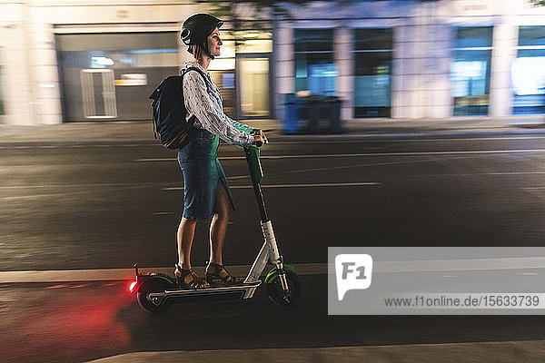 Young woman riding an electric scooter in the city at night  Berlin  Germany