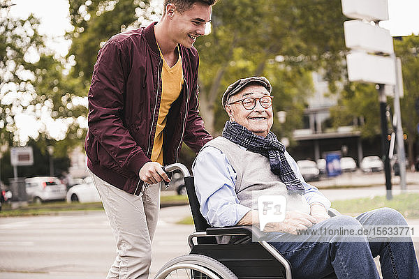 Junger Mann schiebt glücklichen älteren Mann im Rollstuhl
