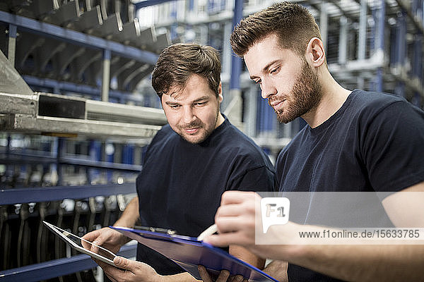 Zwei Arbeiter mit Zwischenablage und Tablette im Fabriklager