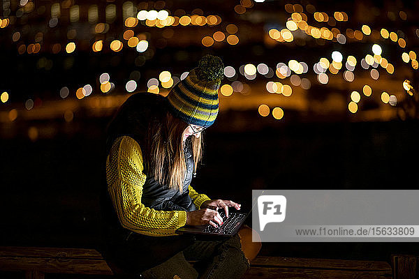 Junge Frau  die nachts im Freien einen Laptop benutzt