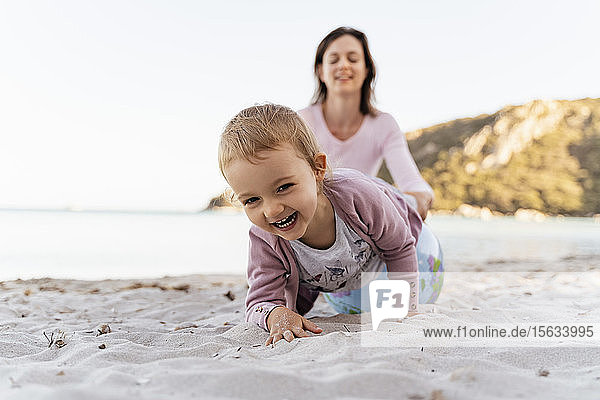 Porträt eines glücklichen kleinen Mädchens  das mit dem Earth-Beachball spielt  während seine Mutter im Hintergrund sitzt