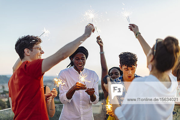 Gruppe glücklicher multiethnischer Freunde feiert am Abend eine Party mit Wunderkerzen