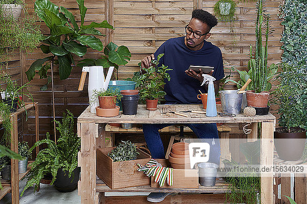 Junger Mann benutzt digitales Tablet auf seiner Terrasse bei der Gartenarbeit
