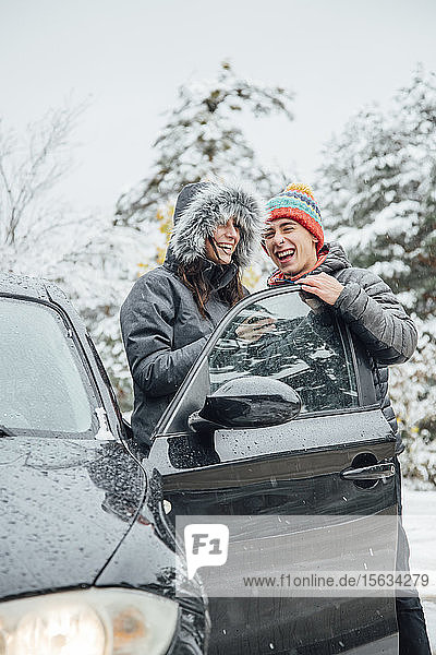 Lachendes junges Paar mit Auto im Winterwald